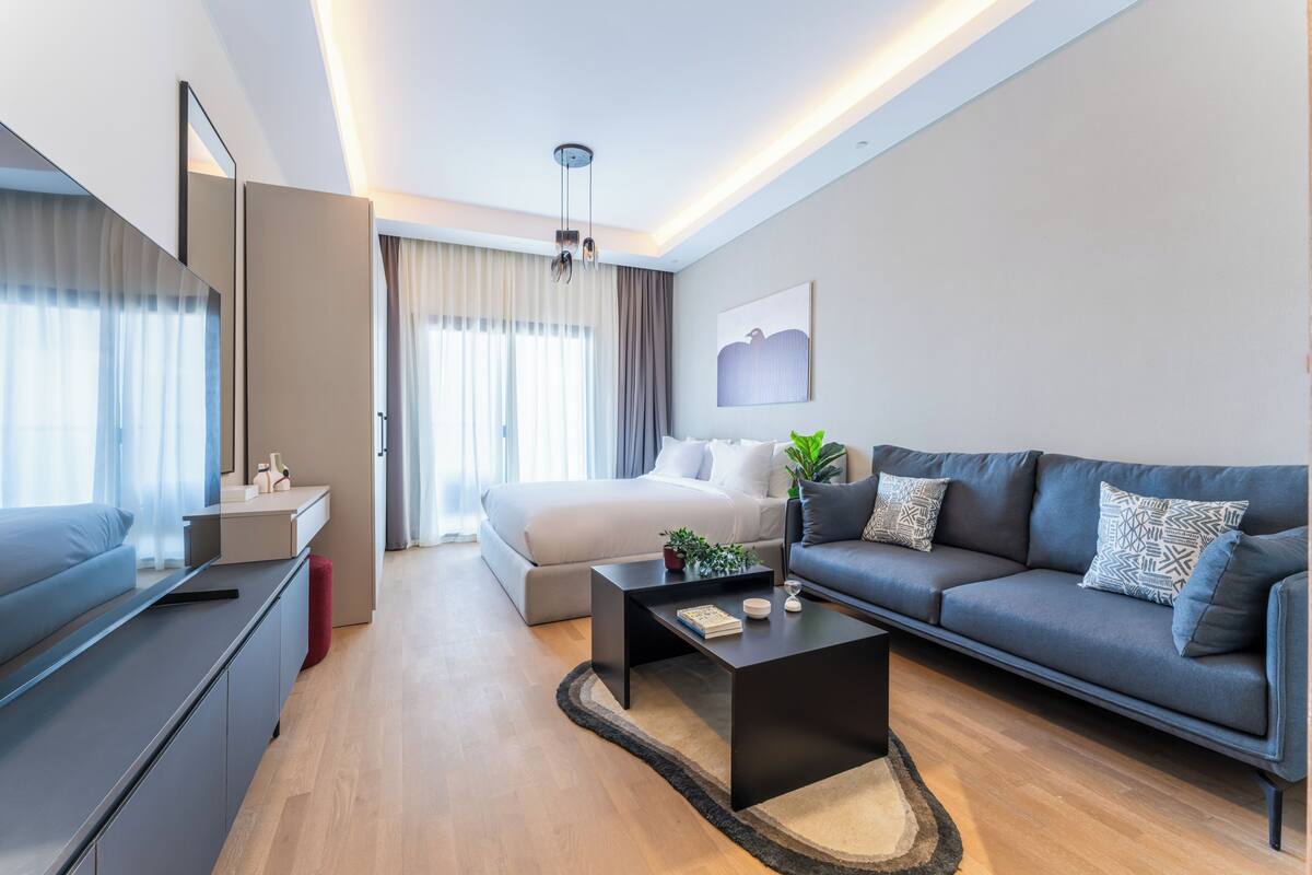 Una habitación de hotel moderna con cama, sofá, mesa de centro y televisor.