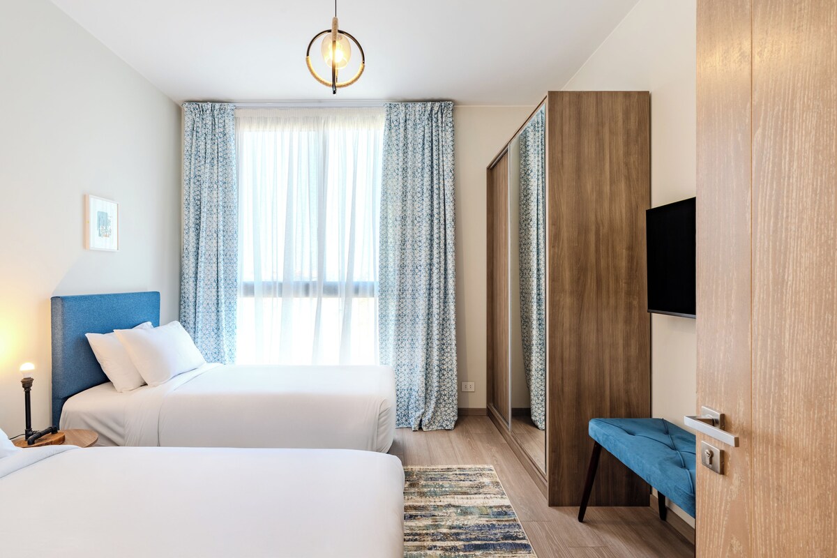 Una habitación de hotel con dos camas, un espejo grande, un televisor y un armario de madera.