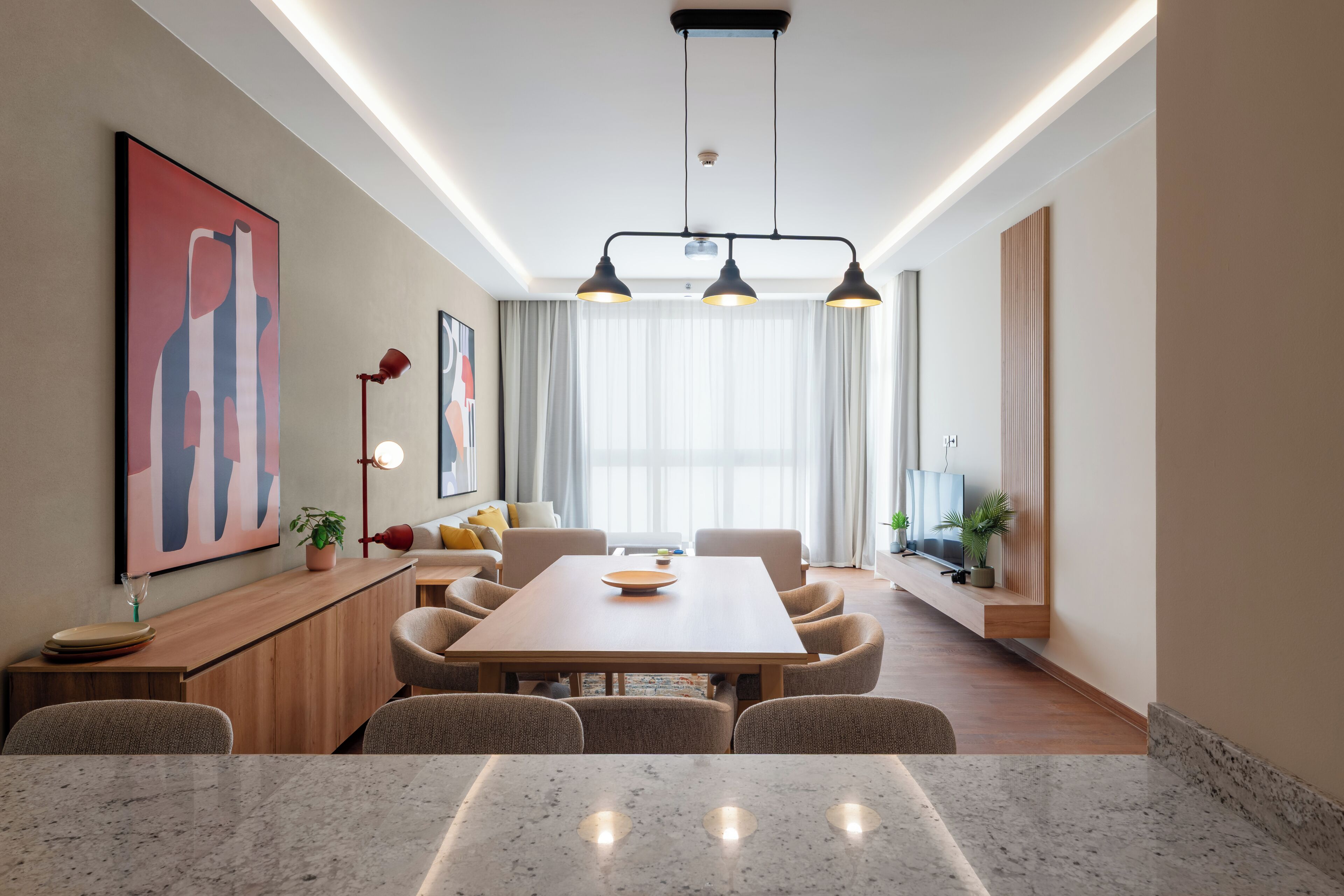 Un comedor moderno con una mesa de madera, sillas, iluminación colgante y obras de arte en las paredes.