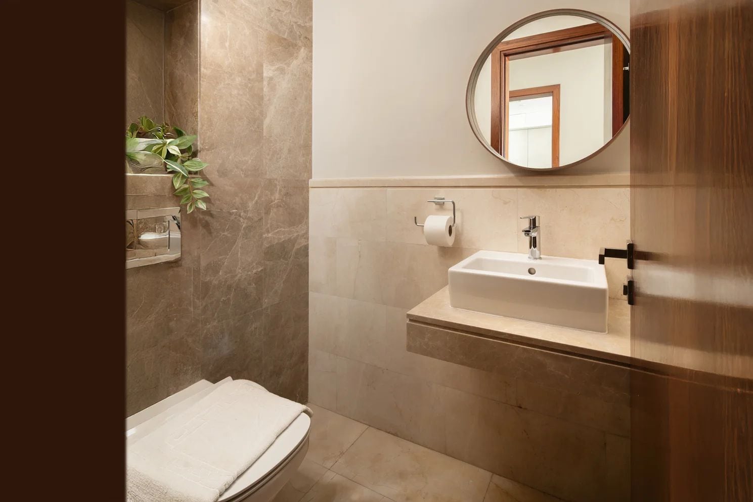 Une salle de bain avec un mur en marbre, un lavabo avec un miroir, une serviette et une plante.