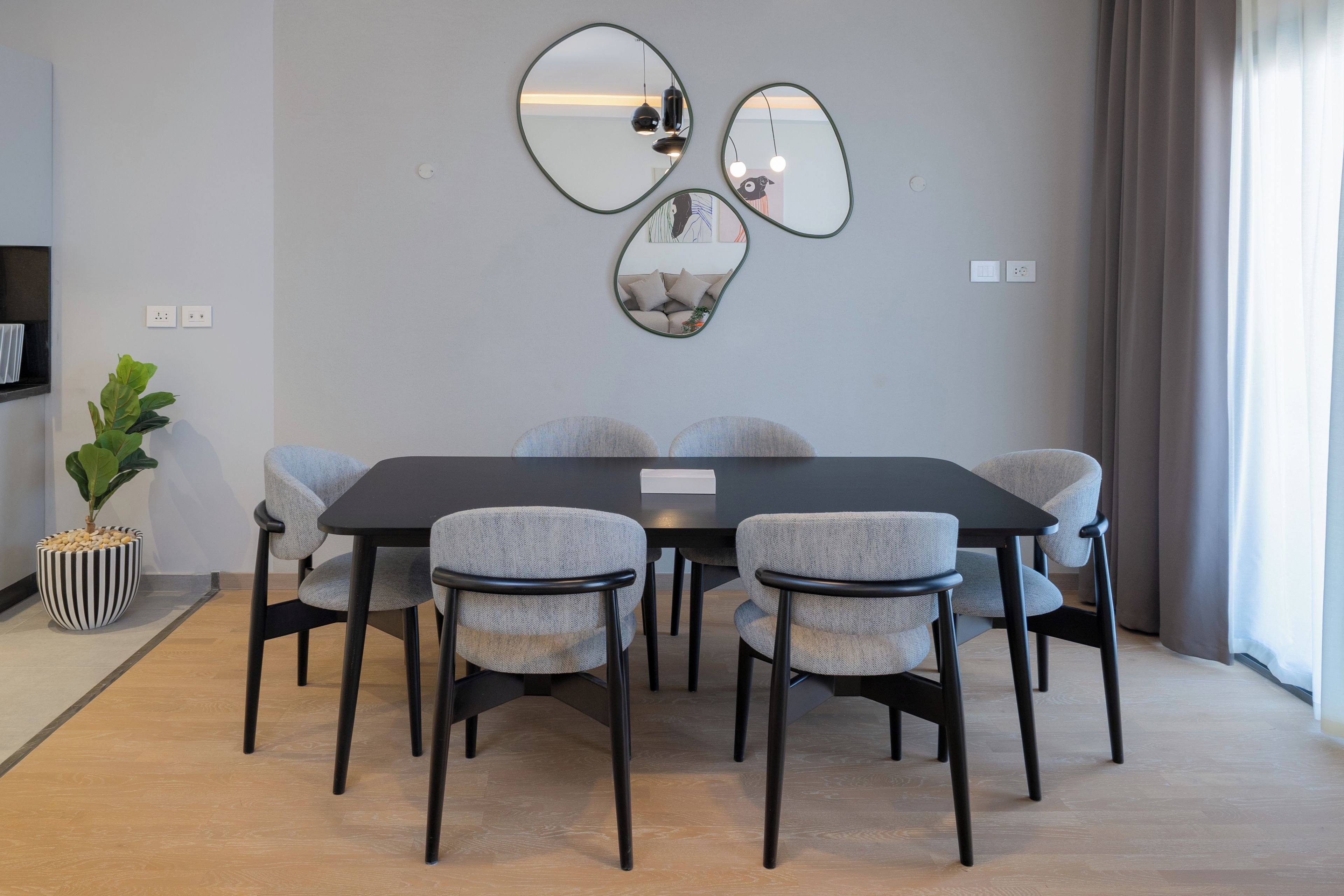 A modern dining area with a rectangular table, six chairs, and three wall-mounted mirrors.
