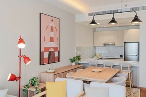 A modern kitchen with a stainless steel refrigerator, a wooden dining table, and a red pendant light.