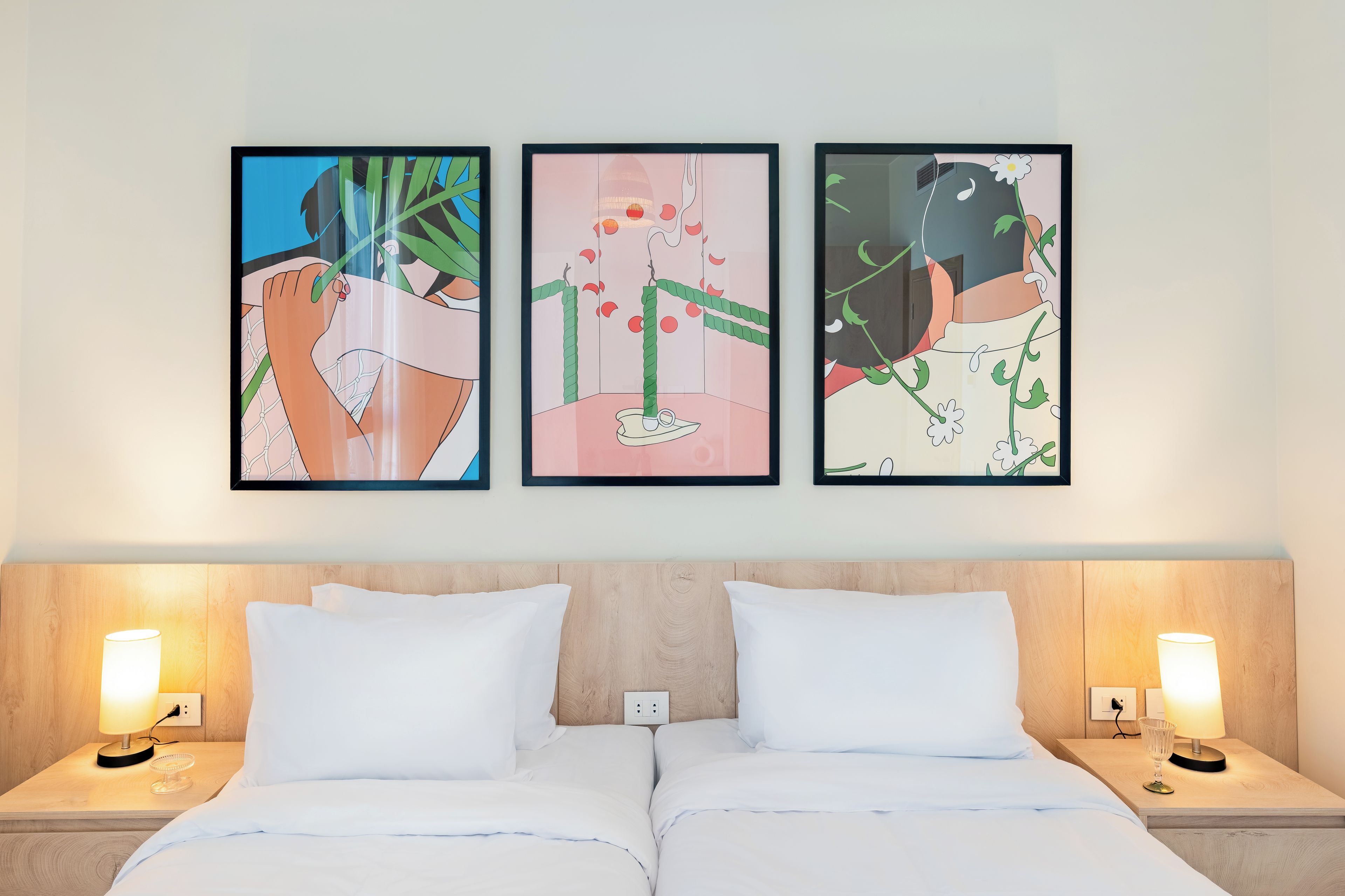 Une chambre d’hôtel avec un lit, deux tables de chevet avec des lampes et trois œuvres d’art encadrées accrochées au mur.