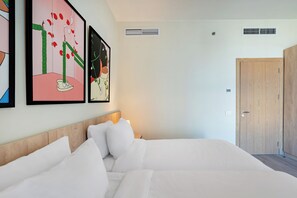 Una habitación de hotel con una cama, cabecera de madera, una puerta y dos rejillas de ventilación en la pared.