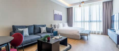 A modern hotel room with a sofa, a bed, a dining table, and a TV.