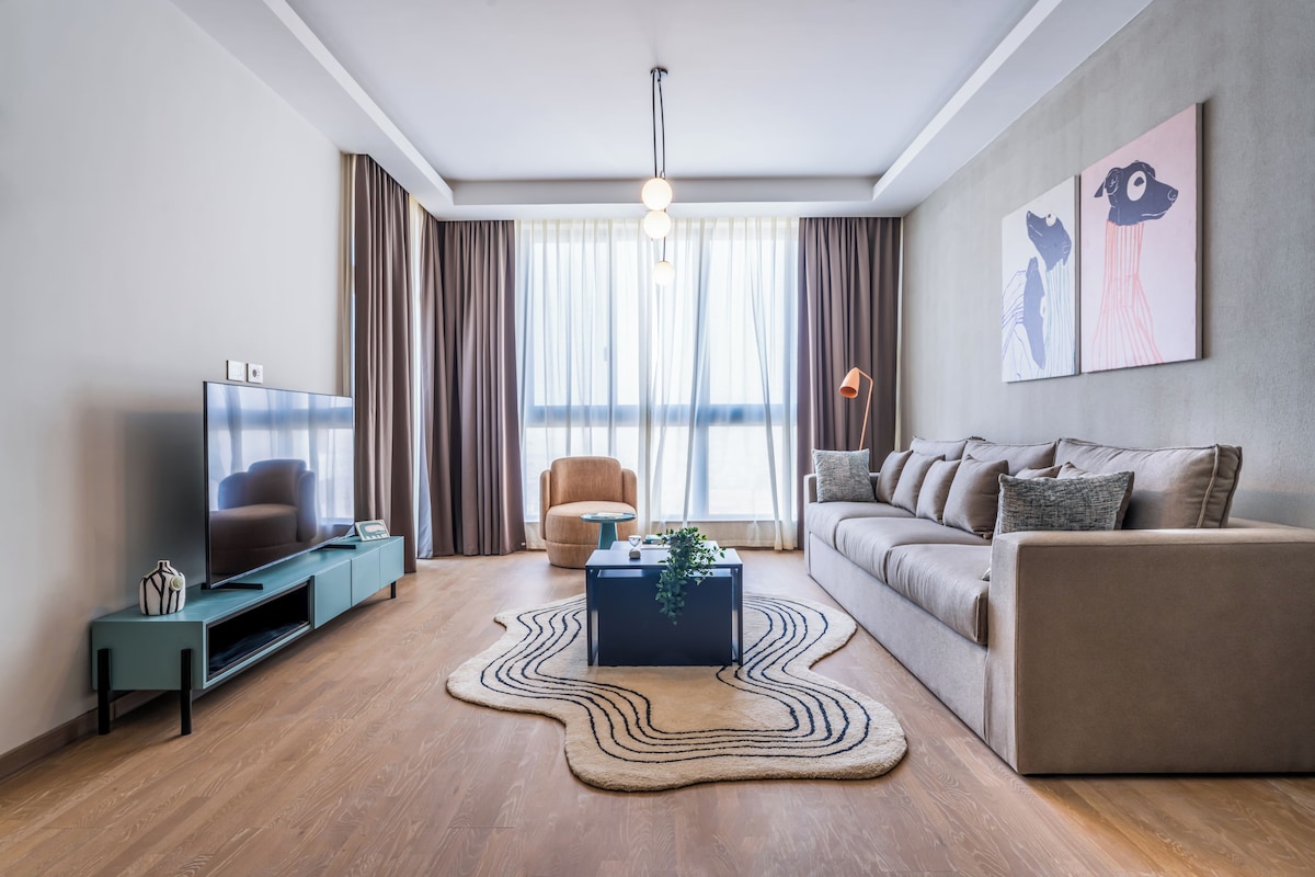 A modern living room with a flat-screen TV, a sofa, a coffee table, and a decorative rug.