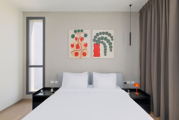 A modern hotel room with a large bed, two bedside tables, a nightstand, a window, and two abstract wall art pieces.