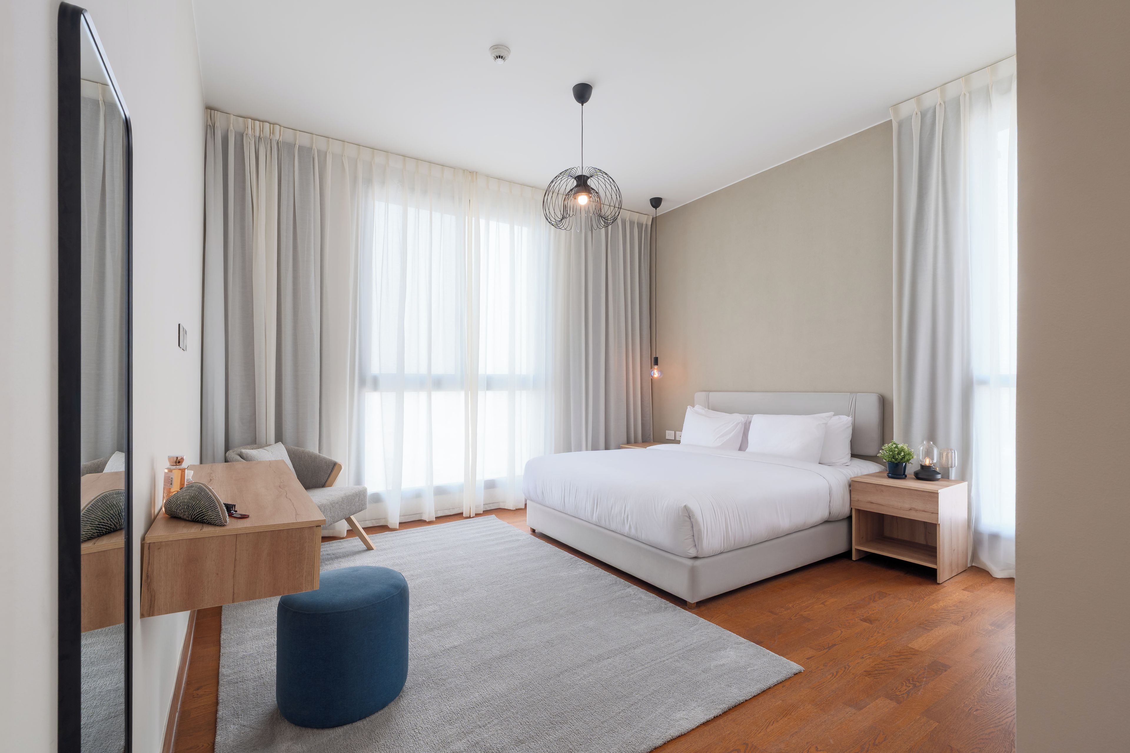 A modern bedroom with a large bed, a desk, and a mirror.