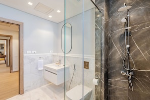 A modern bathroom with a glass-enclosed shower, a white sink, and a marble-tiled wall. - Brassbell Sheikh Zayed Aeon Towers (6th of October City)