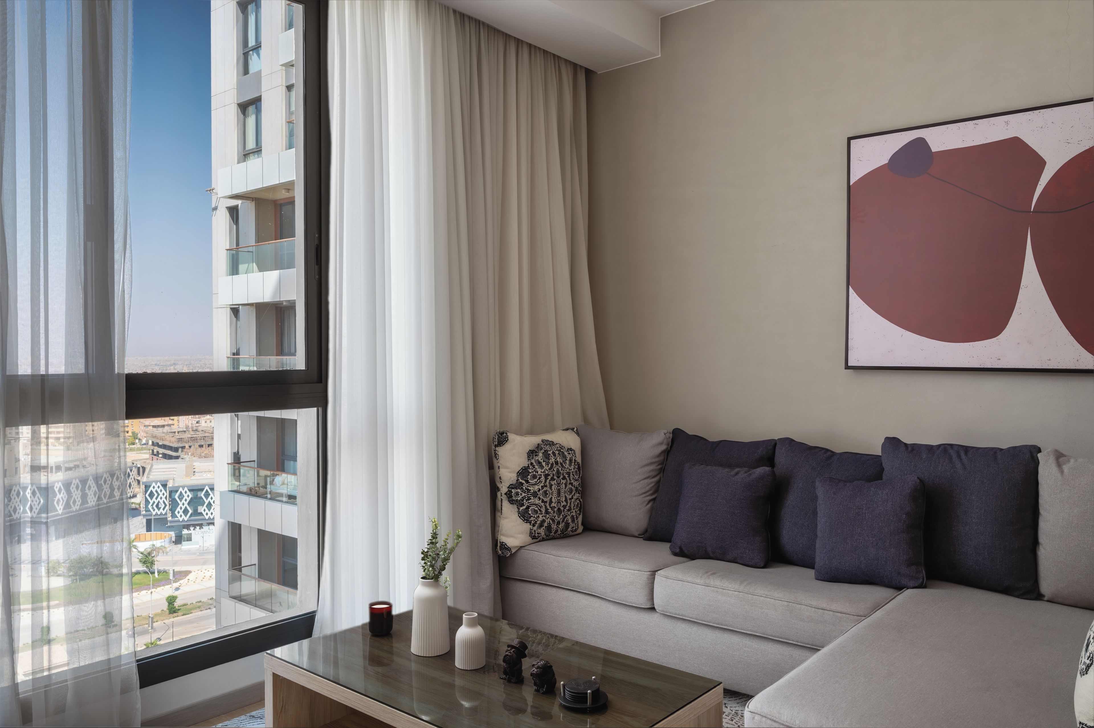 A modern living room with a sofa, a coffee table, and a large window with curtains.