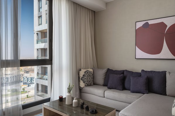 A modern living room with a sofa, a coffee table, and a large window with curtains.