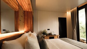 A modern bedroom with a large bed, wooden headboard, bedside table, and a view of greenery outside. - Leona Valley View Ubud (Ubud)