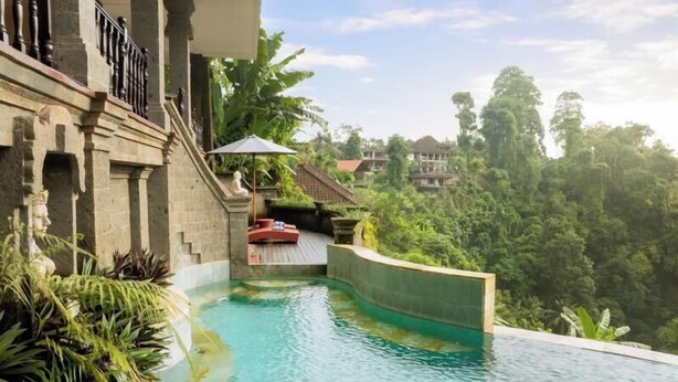 A swimming pool with a stone wall, a red lounge chair, and lush greenery in the background. - Leona Valley View Ubud (Ubud)