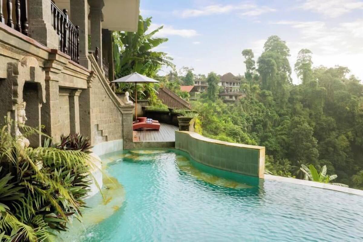 A swimming pool with a stone wall, a red lounge chair, and lush greenery in the background.
