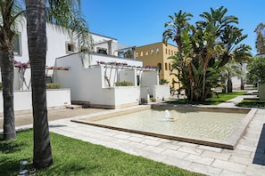 Un patio con fuente, palmeras y un edificio blanco con pérgola.
