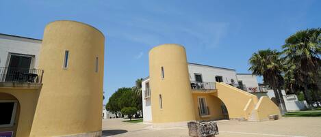A courtyard with yellow cylindrical structures, a stone bench, and a white building with balconies.