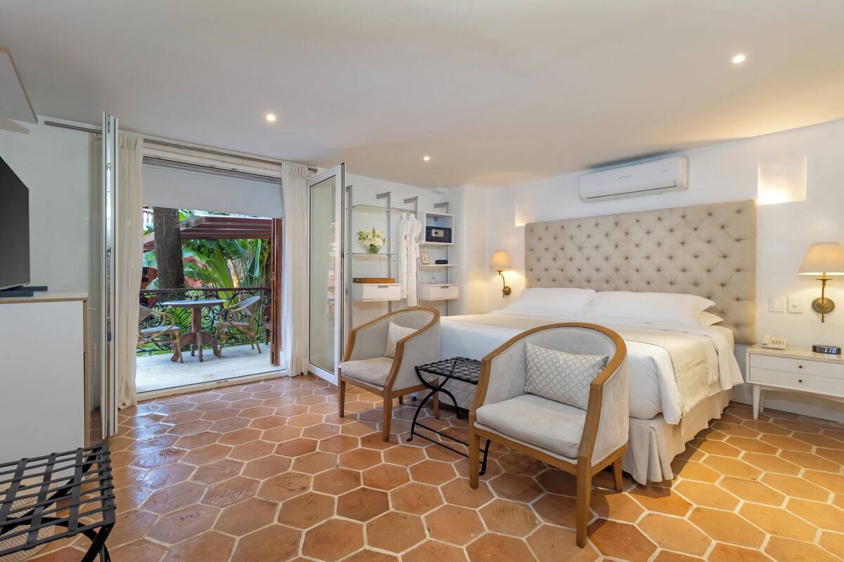 Une chambre d’hôtel avec un lit, deux chaises, une table de chevet et une petite table.