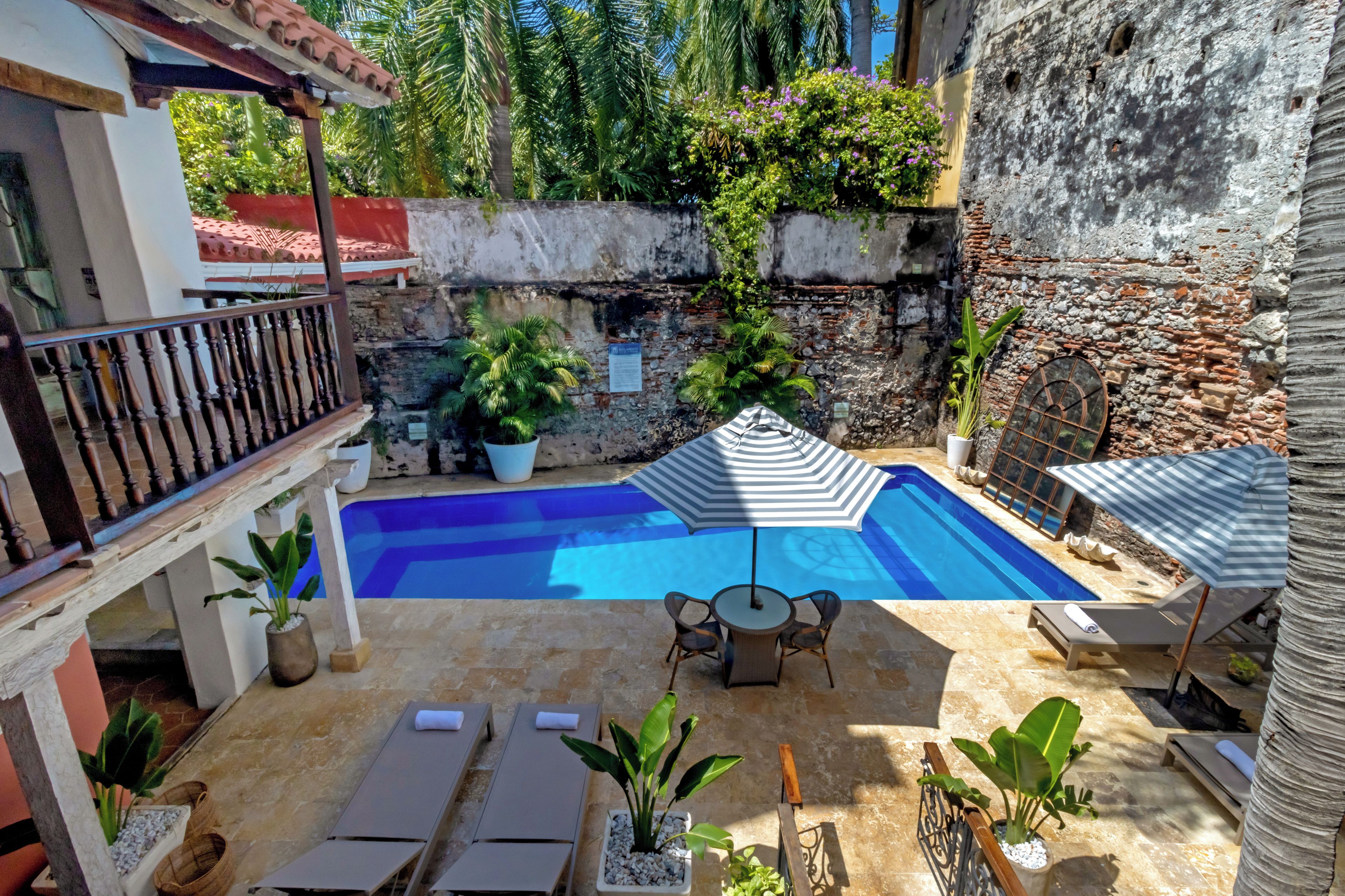 Une piscine entourée de chaises longues et de parasols, agrémentée de plantes en pot et d’un mur de pierre.