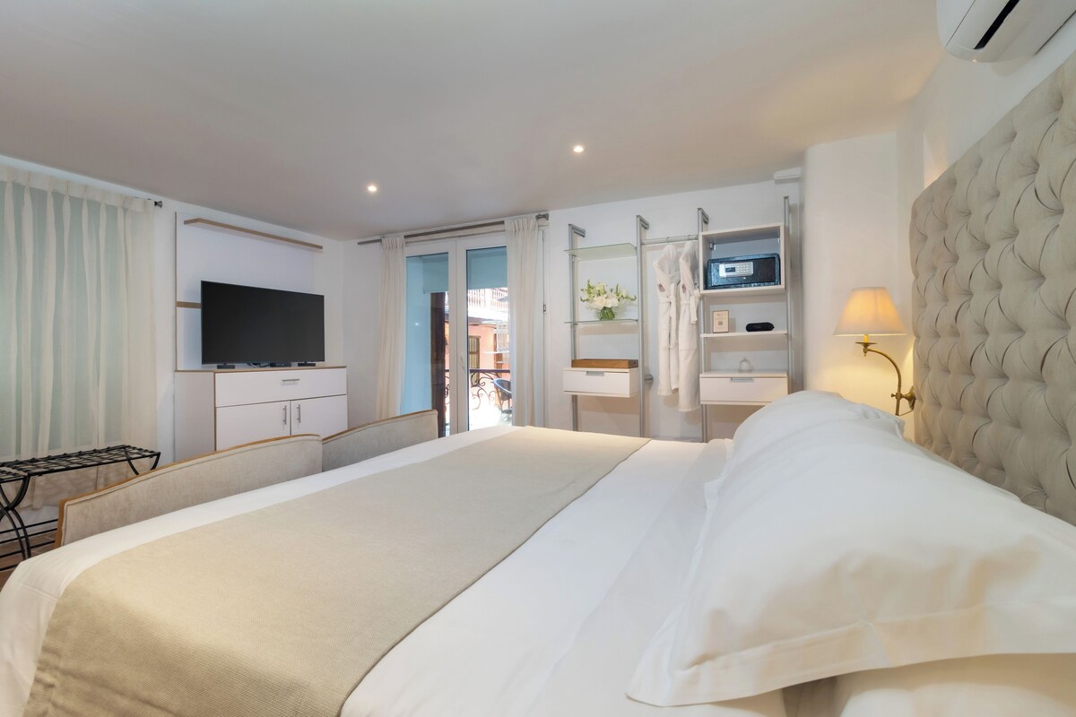 Een hotelkamer met een groot bed, een televisie, een garderobe, een badkamer met spiegel en een raam.