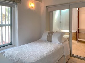 Quarto com cama, janela e porta deslizante para um banheiro.