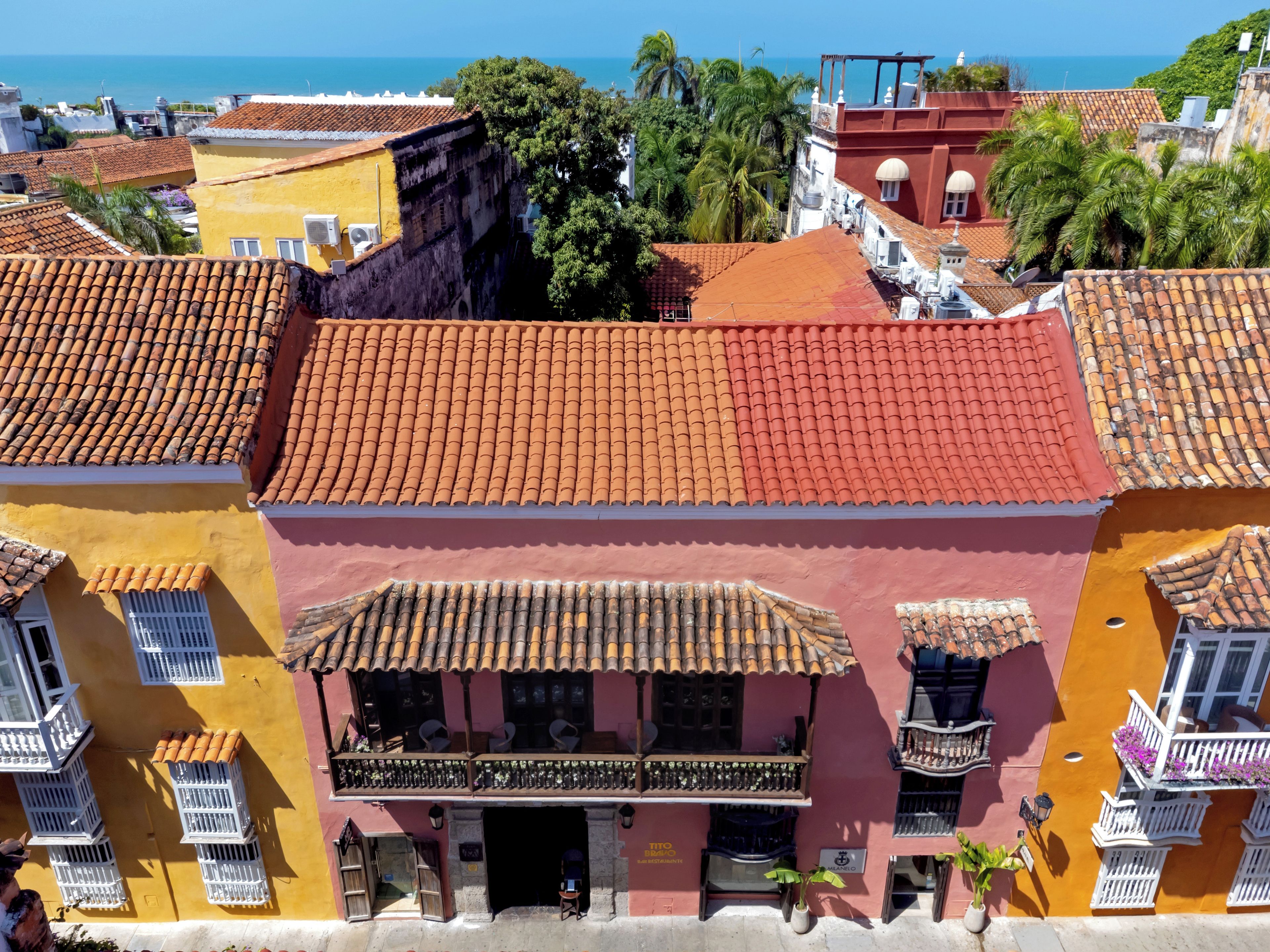 A colorful building with a red-tiled roof, balconies, and a view of the sea.