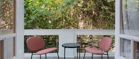A balcony with two chairs and a table, surrounded by a white railing, with a view of dense foliage.