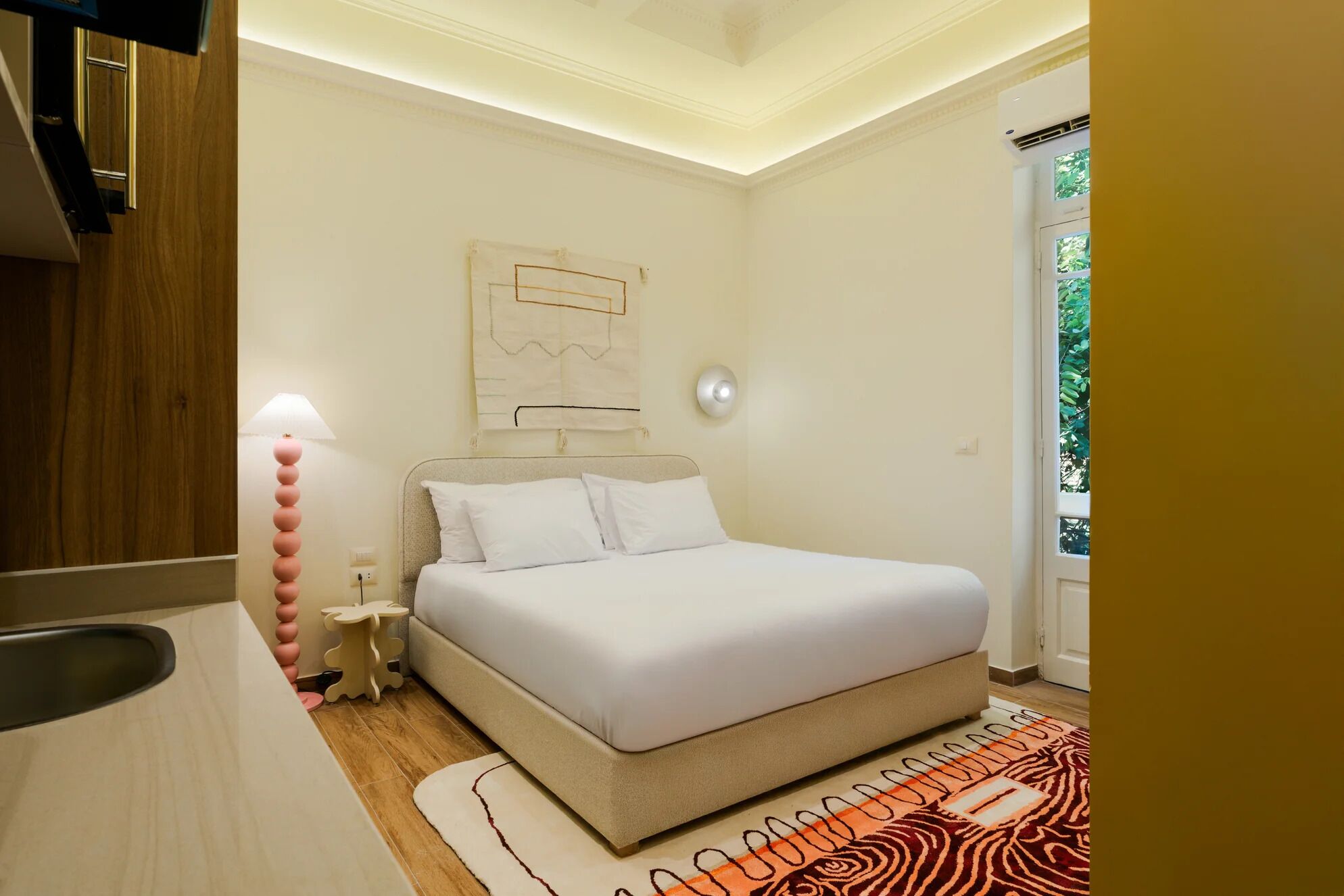 A bedroom with a bed, bedside table, lamp, and a wall-mounted artwork.