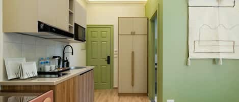 A compact kitchen with a microwave, sink, and cabinets, a green door, and a bed with a simple headboard.