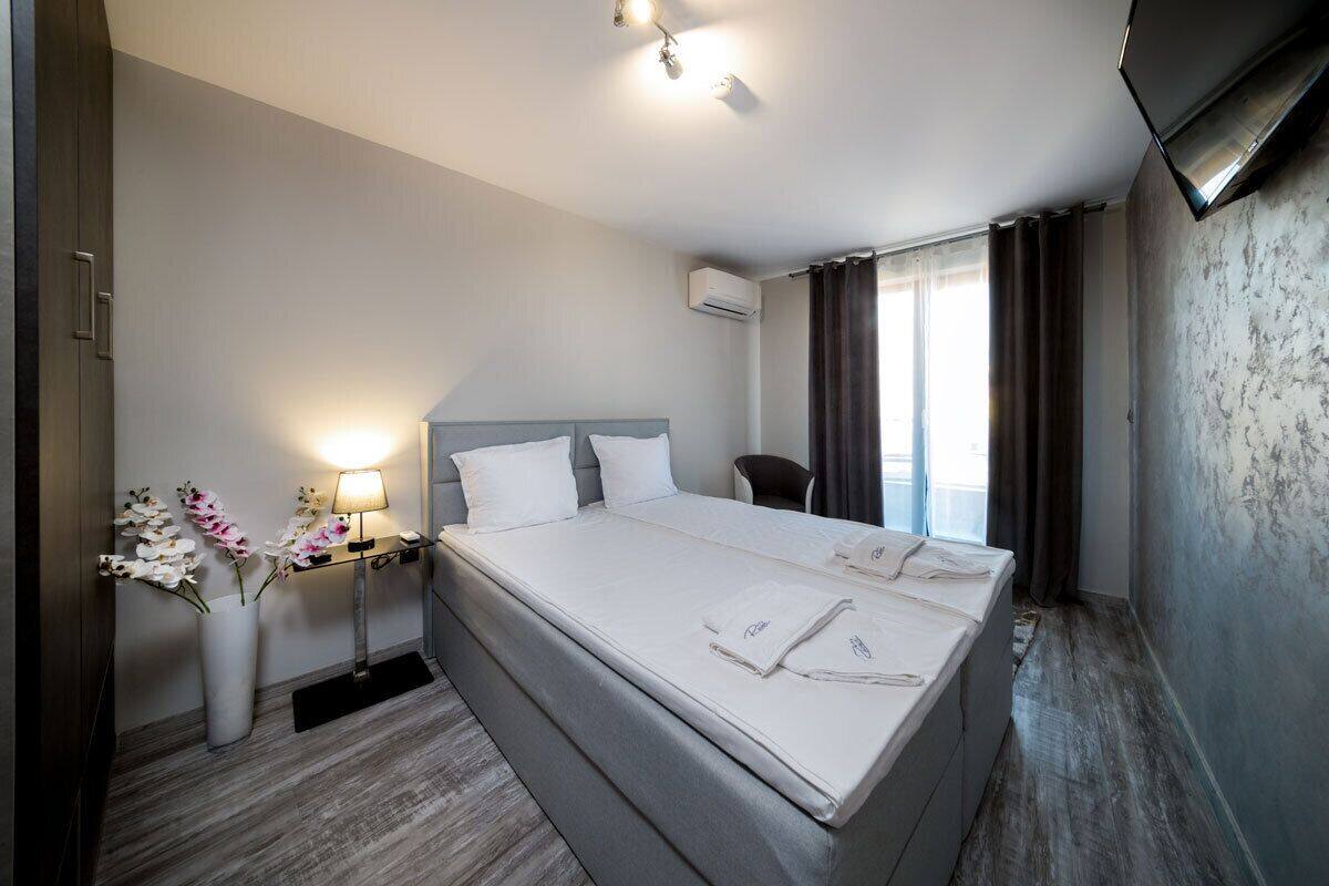 A hotel room with a large bed, a bedside table with a lamp, a chair, and a TV mounted on the wall.