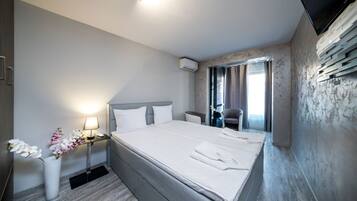 Una habitación de hotel con una cama grande, mesitas de noche, televisión y ventana con cortinas.