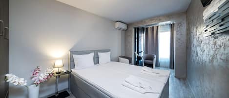 Una habitación de hotel con una cama grande, mesitas de noche, televisión y ventana con cortinas.