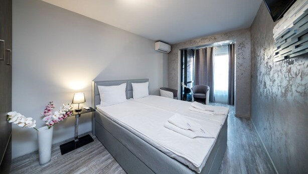 A hotel room with a large bed, bedside tables, a TV, and a window with curtains.