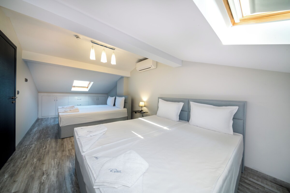 A modern hotel room with a large bed, a smaller bed, a skylight, and a ceiling fan.