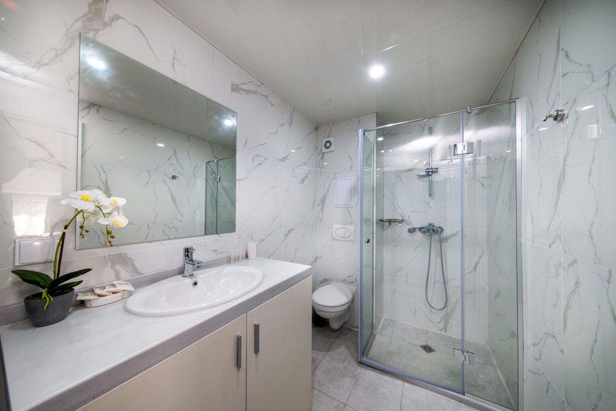 A modern bathroom with a marble vanity, a glass-enclosed shower, and a toilet.
