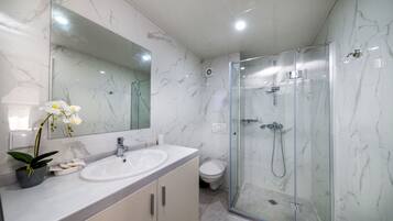 Un baño moderno con tocador de mármol, ducha con cerramiento de vidrio y un inodoro.