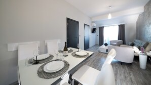 A modern dining area with a white table set for two, a bottle of wine, and a flat-screen TV mounted on the wall.