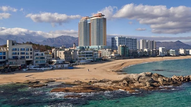 A coastal cityscape with a prominent high-rise hotel, a sandy beach, and rocky shoreline. - Wyndham Goseong Gangwon (Goseong)
