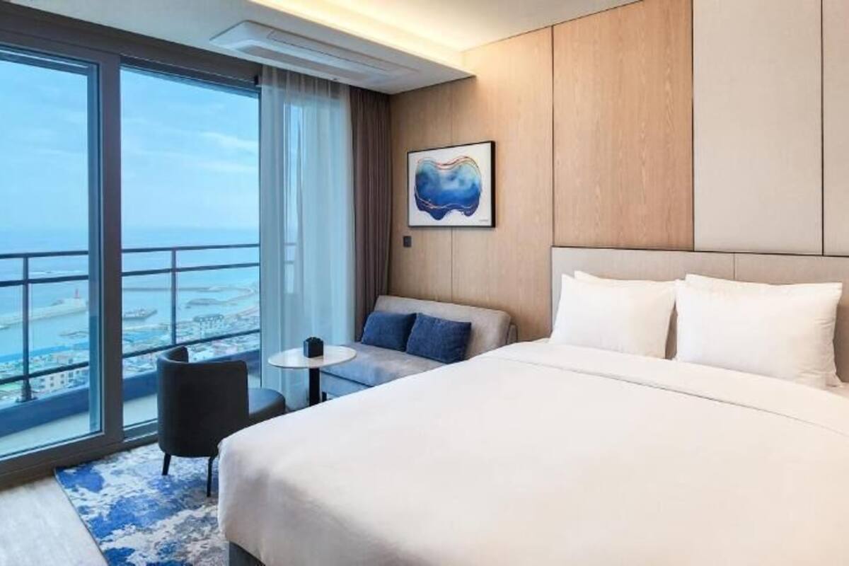 Habitación de hotel con una cama grande, una mesita pequeña, una silla y vistas a la ciudad.