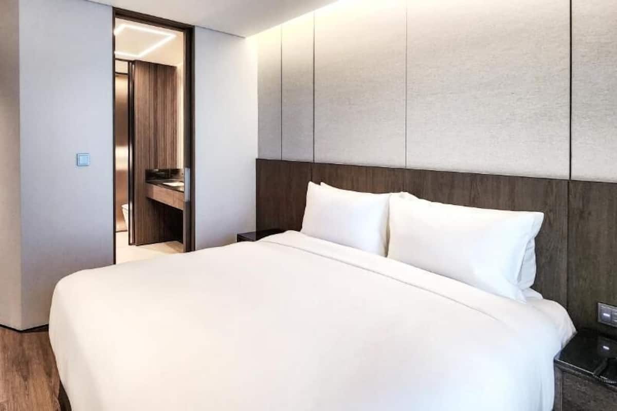 A hotel room with a large bed, a wooden floor, a wardrobe, and a mirror.