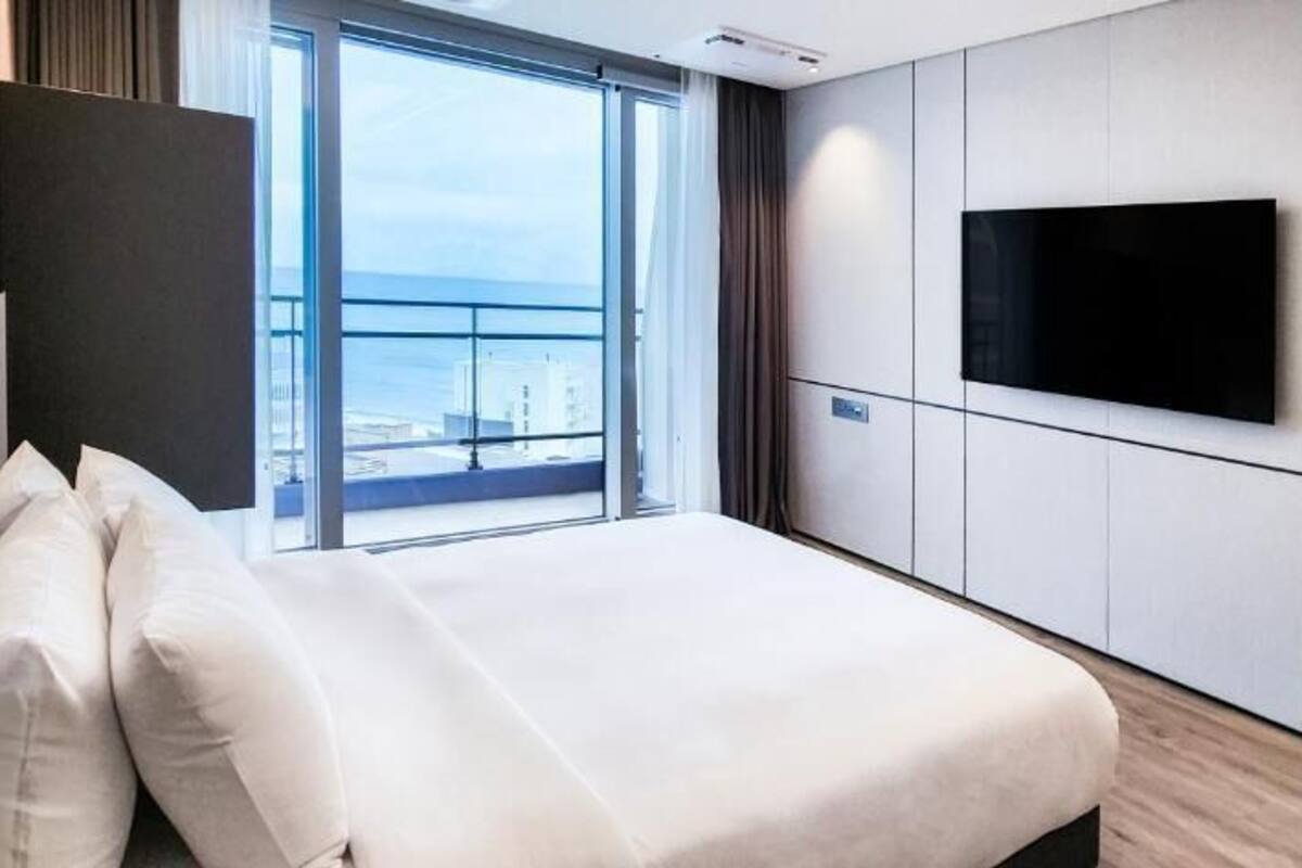 Habitación de hotel con cama, televisor montado en la pared y un amplio ventanal con vistas a la ciudad.