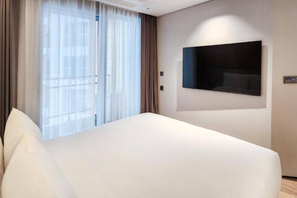 Una habitación de hotel moderna con una cama grande, un televisor de pantalla plana montado en la pared y un ventanal con cortinas.