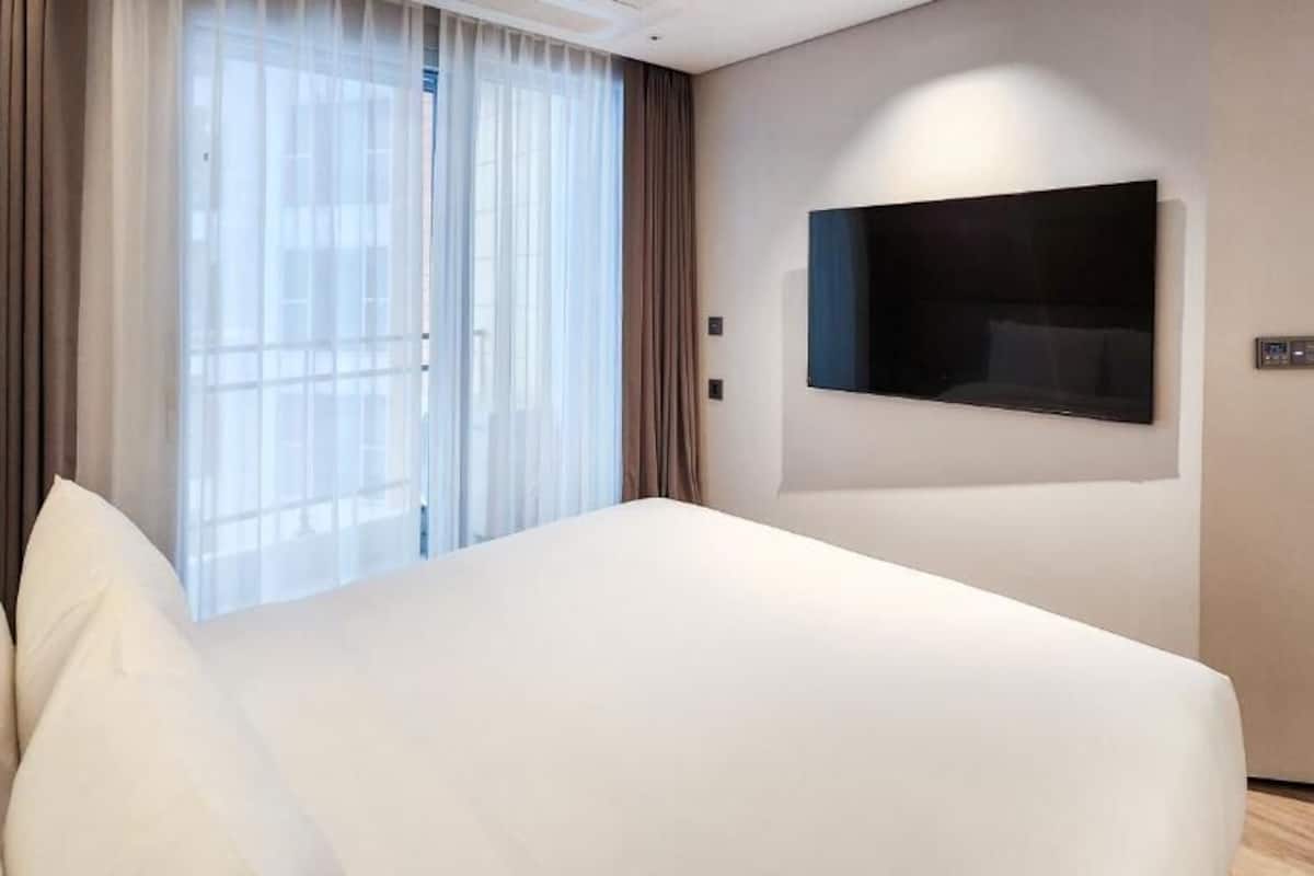 A modern hotel room with a large bed, a flat-screen TV mounted on the wall, and a large window with curtains.
