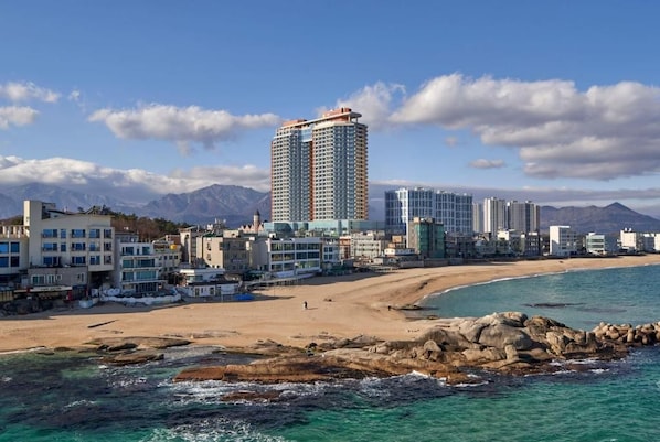 A coastal cityscape with a prominent high-rise hotel, a sandy beach, and rocky shoreline. - Wyndham Goseong Gangwon (Goseong)
