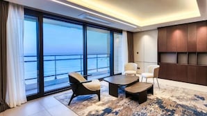 A modern hotel room with a large window offering a view of the sea, a seating area with a coffee table, and a dark wood panel wall. - Wyndham Goseong Gangwon (Goseong)