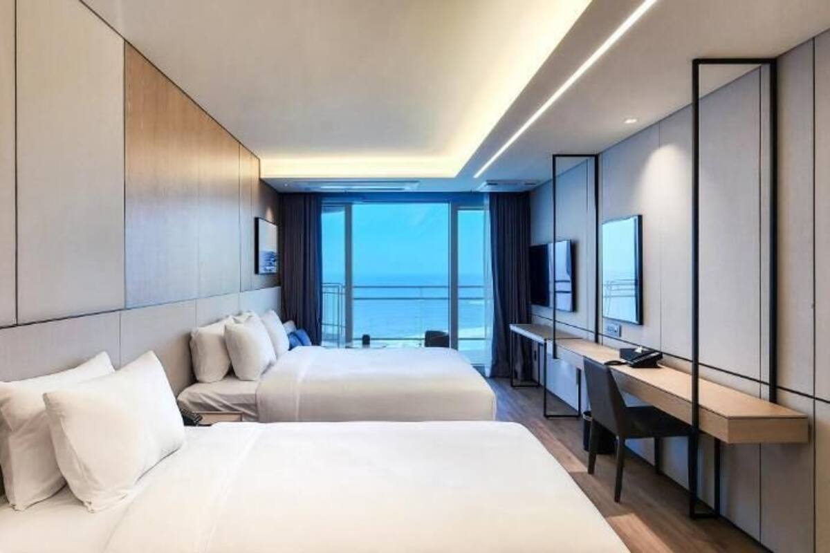 Habitación de hotel moderna con dos camas, un escritorio y un amplio ventanal con vistas al mar.
