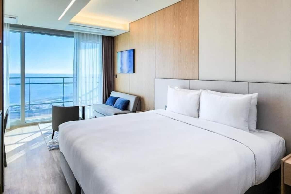 A modern hotel room with a large bed, a desk, and a view of the ocean.