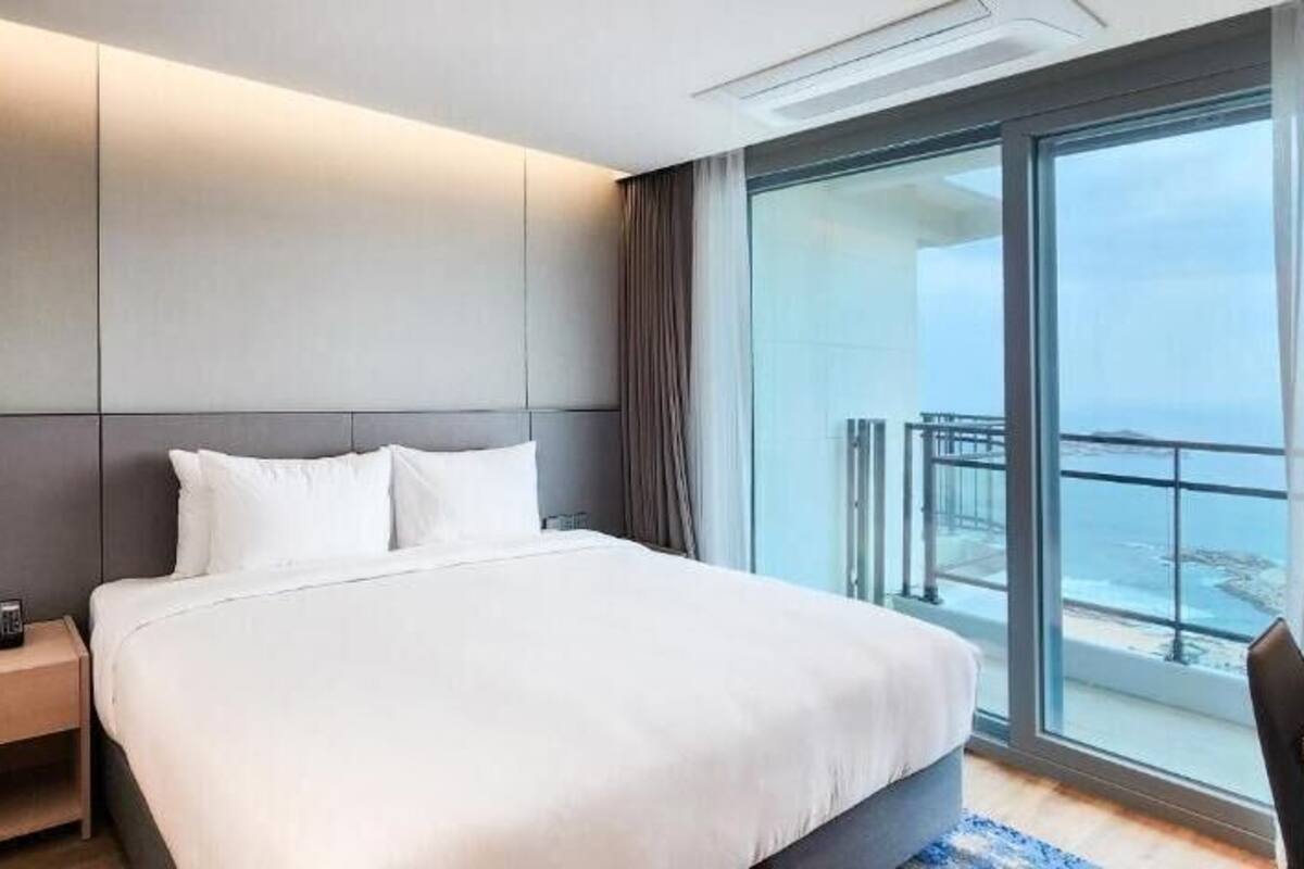 Habitación de hotel con una cama grande, una mesita de noche, un escritorio y un balcón con vistas.