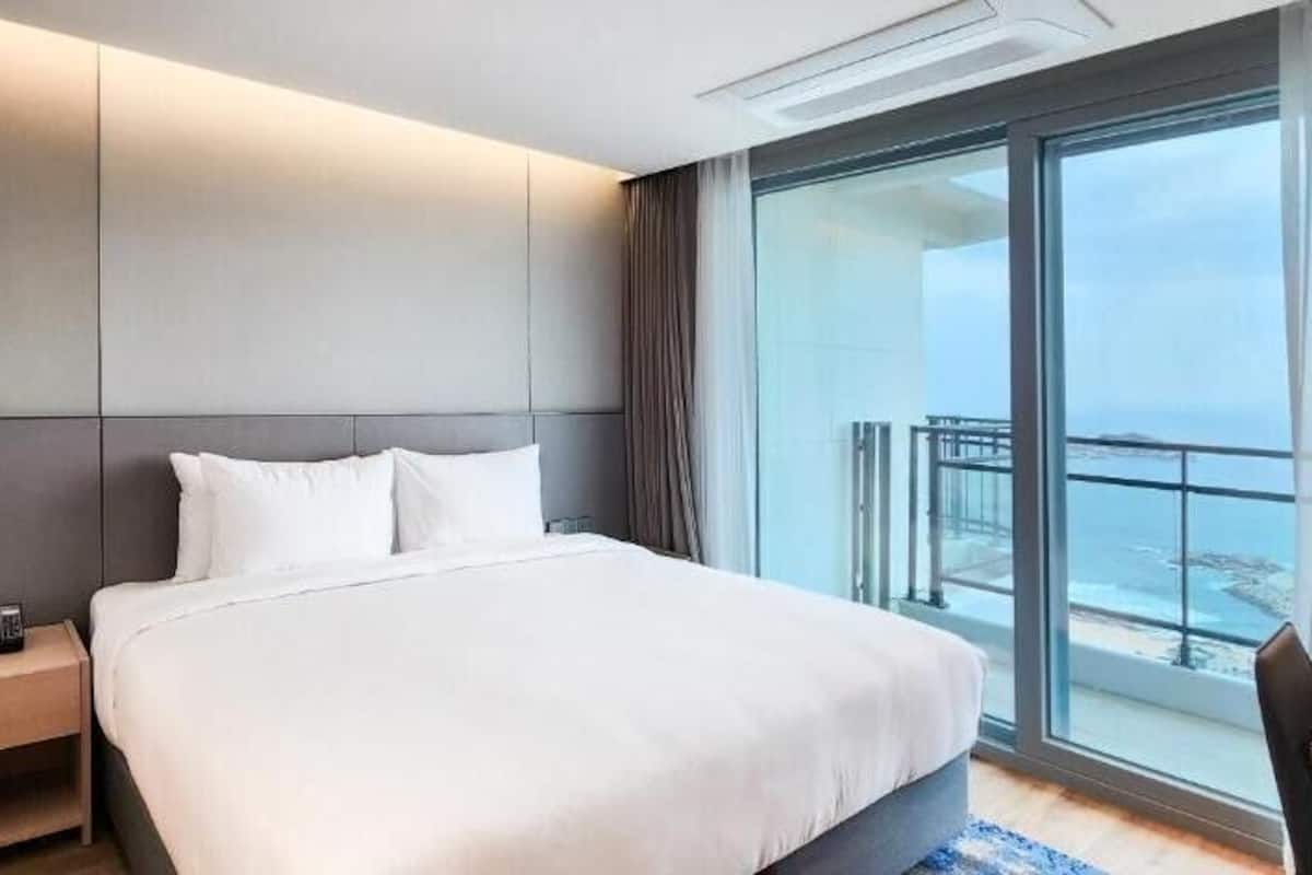 A hotel room with a large bed, a nightstand, a desk, and a balcony with a view.