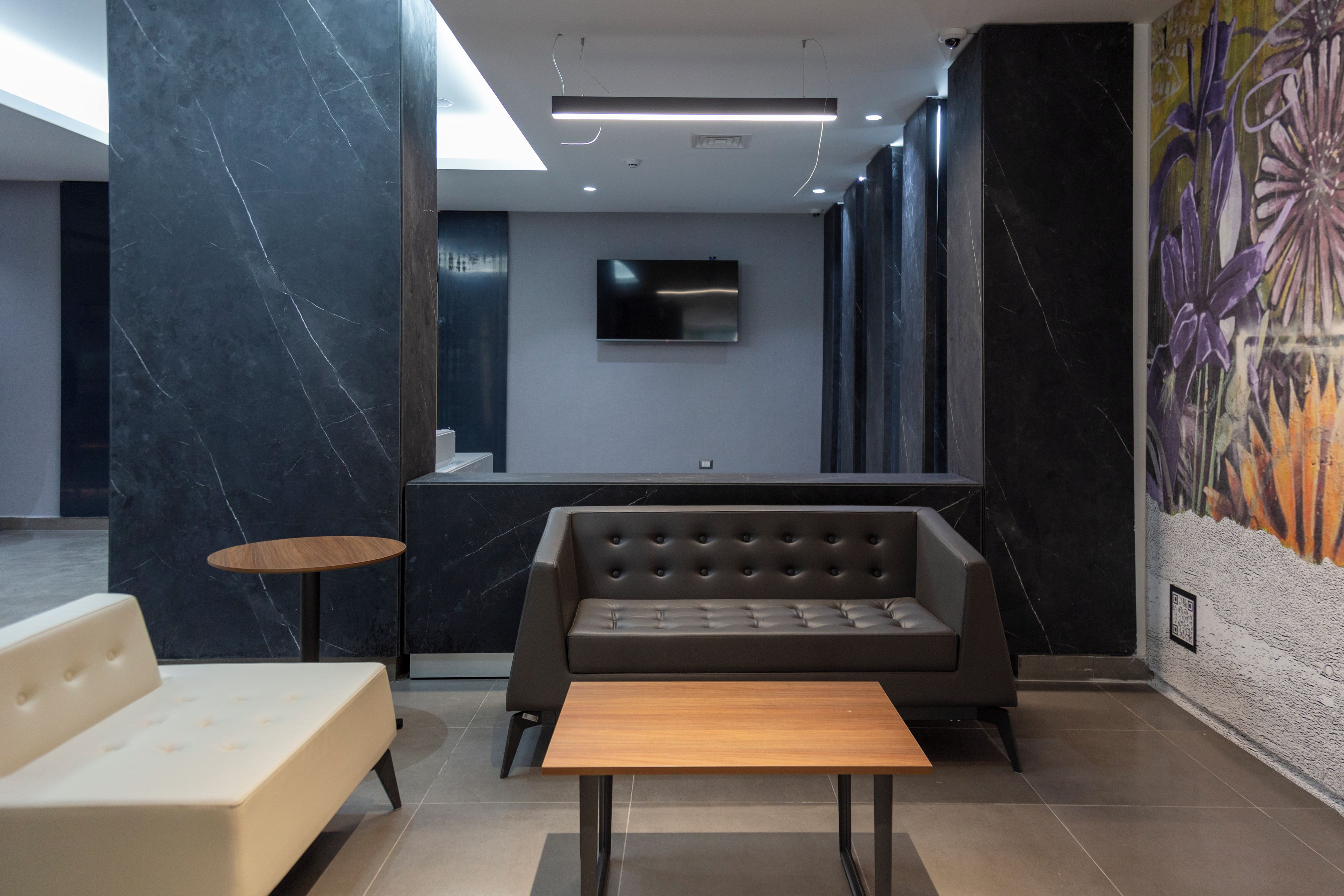 A modern lobby with a sofa, a small table, a TV mounted on the wall, and a mural on the wall.