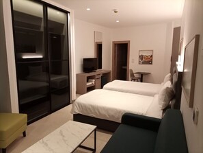 A modern hotel room with two beds, a desk, a chair, and a sliding glass door leading to a balcony. - Liv Weibdeh Hotel Suites (Amman)